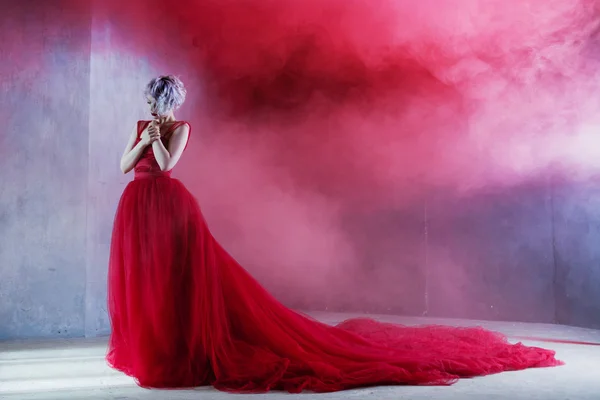 Foto de moda de jovem mulher magnífica em vestido vermelho. Fundo texturizado, fumaça — Fotografia de Stock