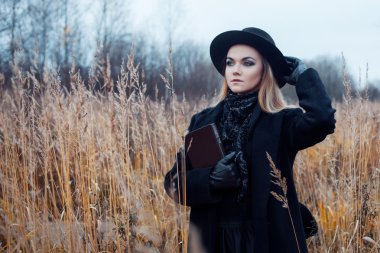 Siyah palto ve şapka genç çekici kadın portresi. Bir alandaki okuma kitabı, sonbahar manzara, kuru ot shes