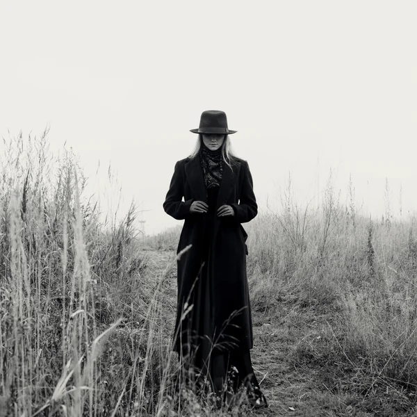 Portrait of young attractive woman in black coat and hat. Autumn landscape, dry grass — Stock Photo, Image