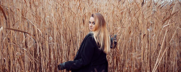 Portret van jonge aantrekkelijke vrouw in zwarte jas en hoed. Herfstlandschap, droog gras — Stockfoto