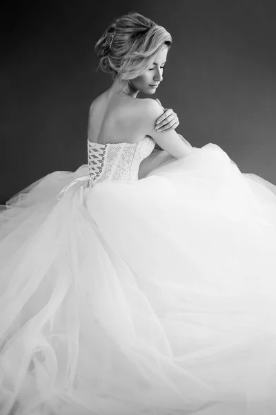 Charmante junge Braut im luxuriösen Hochzeitskleid. hübsches Mädchen in Weiß. grauer Hintergrund. zurück und weißes Foto — Stockfoto