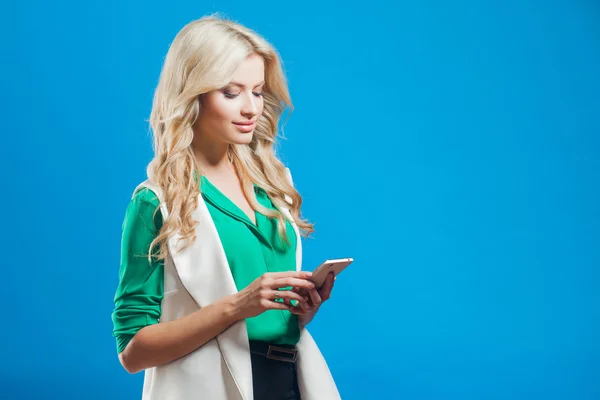 年轻自信的金发女郎的肖像，使用手机，蓝色背景 — 图库照片