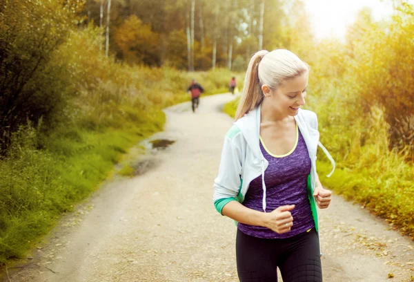 Szczęśliwa i zdrowa dziewczyna runner na drodze z innymi biegaczami w oddali — Zdjęcie stockowe