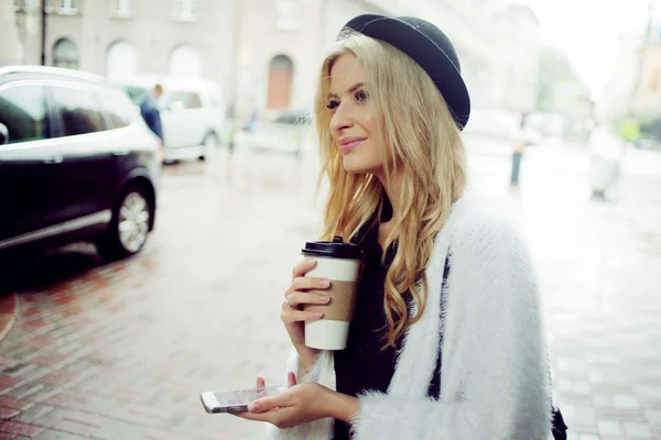 Femme gaie dans la rue buvant du café le matin et utilisant son smartphone . — Photo