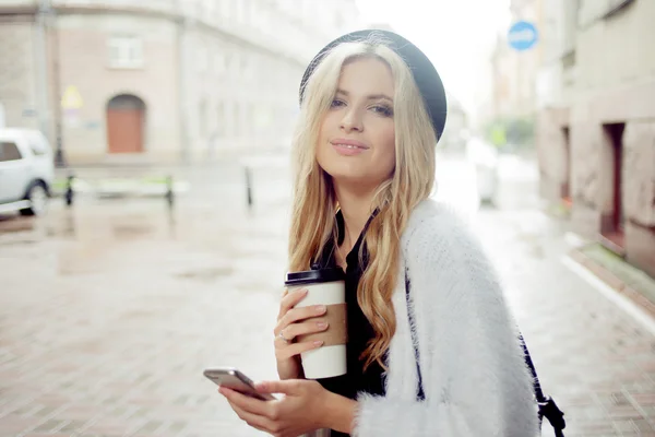 Femme gaie dans la rue buvant du café le matin et utilisant son smartphone . — Photo