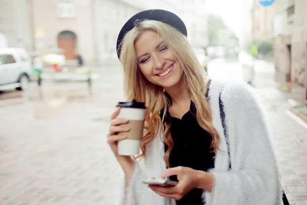 Cheerful woman in the street drinking morning coffee and use her smartphone. — Stock Photo, Image