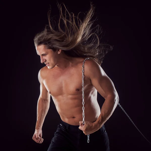 Um jovem com cabelo comprido a arrastar algo para trás. Forte. . — Fotografia de Stock