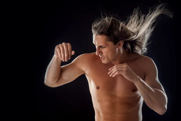 Muskulöser Mann mit langen Haaren, die Hände in der Faust, schwarzer Hintergrund — Stockfoto