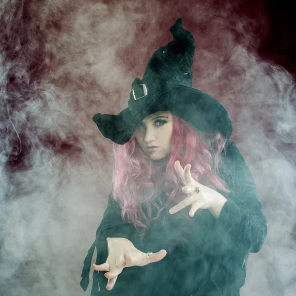 Attractive woman in witches hat with red hair performs magic. Smoke and witchcraft — Stock Photo, Image