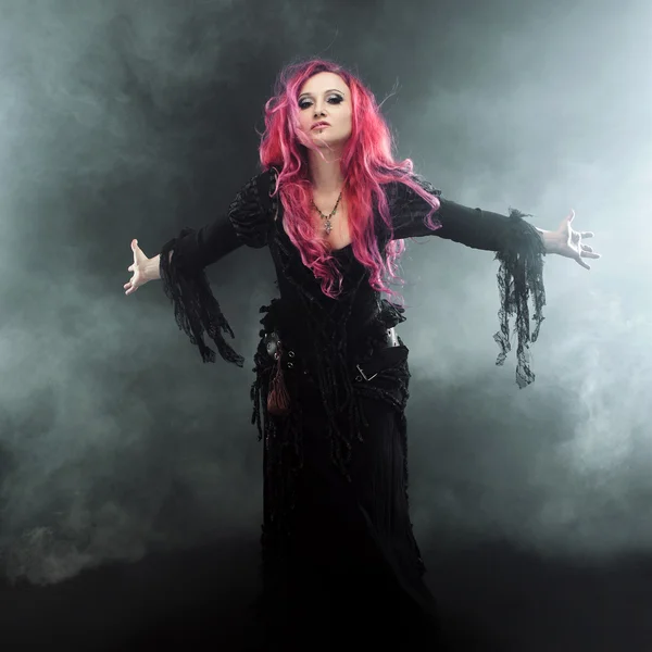 Хэллоуинская ведьма творит магию. Привлекательная женщина с рыжими волосами в костюме ведьмы, вытянутые руки, сильный ветер — стоковое фото