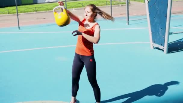 Juggling weights. Young female athlete doing workout, training with a kettlebell in the open air. — Stock Video
