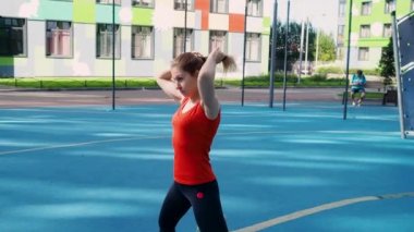Bir atlet sokak sporları sahasında gerinir. Genç bayan sporcu antrenman yapıyor, bir su ısıtıcıyla antrenman yapıyor.