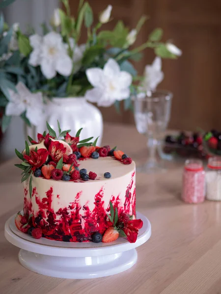 Gyönyörű vörös bársony torta, virágokkal és bogyókkal a tetején. Desszert a konyhaasztalon.. — Stock Fotó