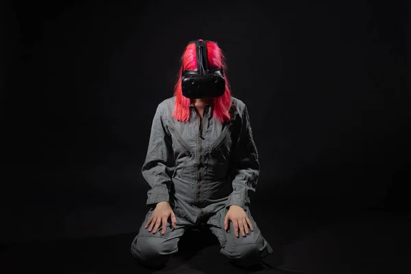 Young woman with pink hair and in a jumpsuit uses virtual reality glasses, is in the game, — Stock Photo, Image