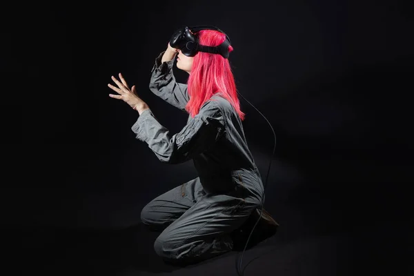 Jovem mulher com cabelo rosa e em um macacão usa óculos de realidade virtual, está no jogo, — Fotografia de Stock