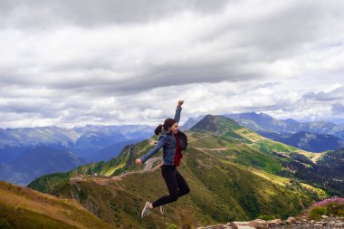 Başarılı bir yürüyüşten sonra neşeli genç kadın dağın tepesine atlıyor..