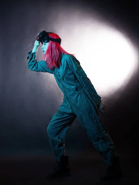 Mujer joven con el pelo rosa y en un mono utiliza gafas de realidad virtual, está en el juego, —  Fotos de Stock