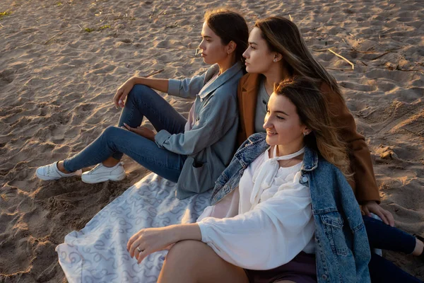 Grupo de mujeres jóvenes en un picnic en la playa, disfrutando de la puesta de sol. Reunión con amigos, — Foto de Stock