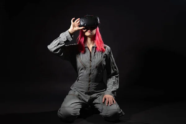 Mladá žena s růžovými vlasy a v kombinéze používá brýle virtuální reality, je ve hře, — Stock fotografie