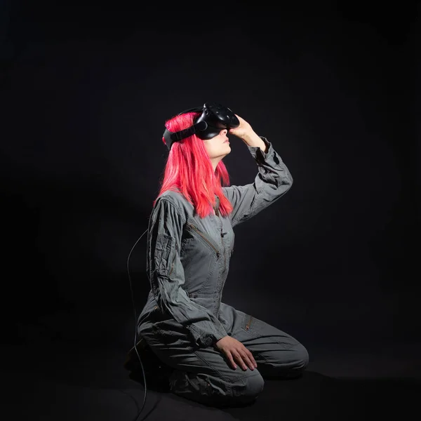 Jovem mulher com cabelo rosa e em um macacão usa óculos de realidade virtual, está no jogo, — Fotografia de Stock