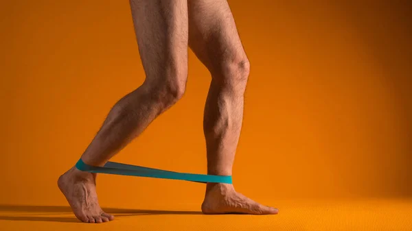 フィットネスのための弾性バンドを持つ筋肉の男性の足は、足の筋肉を緊張させる演習を行う. — ストック写真