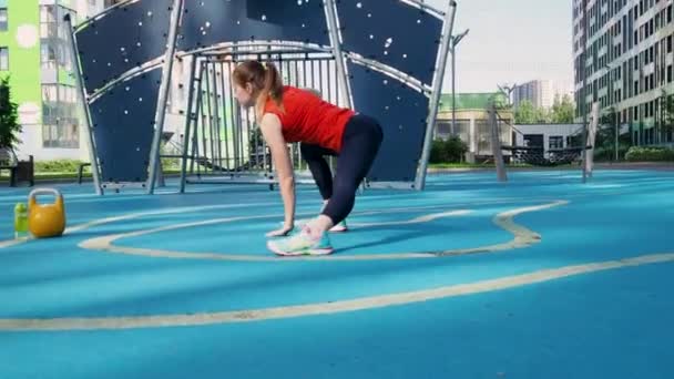 Un athlète fait un étirement sur un terrain de sport de rue. Jeune athlète féminine faisant de l'entraînement, s'entraînant avec une kettlebell — Video