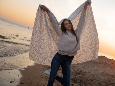 Genç ve güzel bir kadın sıcak bir battaniyeye sarılmış, kumsalda sıcak ve samimi..