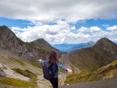 Bir dağ panoramasının arka planında genç bir bayan turist. Kollarını açarak ayakta duruyor.,