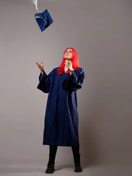 Happy graduate on a gray background. A young woman with bright hair