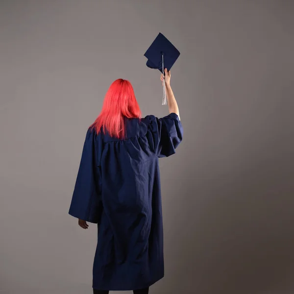 Happy graduate on a gray background. A young woman with bright hair