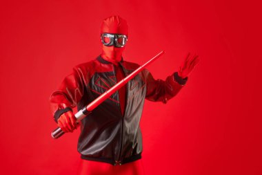 Kırmızı taytlı ve koruyucu gözlüklü komik süper kahraman oyuncak kılıç kullanıyor..