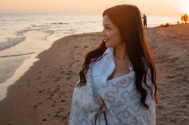 Genç ve güzel bir kadın sıcak bir battaniyeye sarılmış, kumsalda sıcak ve samimi..