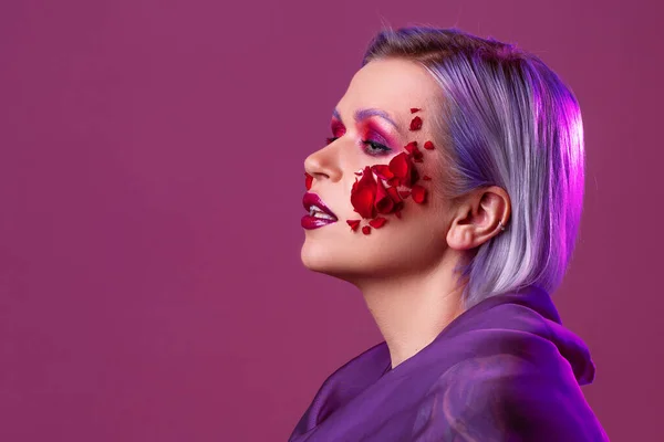 Elegante e luminosa giovane donna con trucco colorato e petali di fiori sul viso — Foto Stock