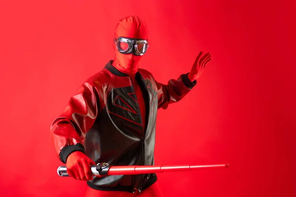 Super herói engraçado em um colete vermelho e óculos de proteção usa uma espada de brinquedo. — Fotografia de Stock