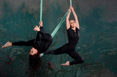 Dar siyah eşofmanlı iki güzel kadın süspansiyonda yoga yapıyor.,