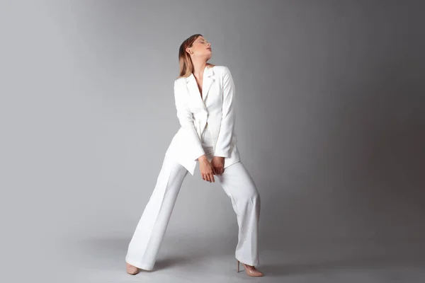 Mooie jonge vrouw in een trendy wit pak staat in een dynamische pose, — Stockfoto