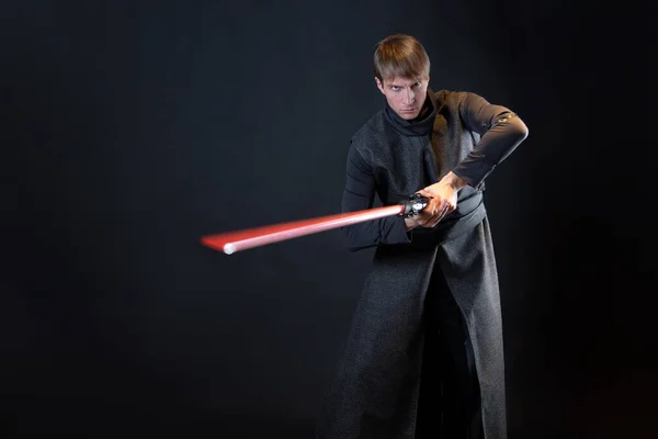 A villain with a red lightsaber, a young man in a long robe does fighting poses, — Stock Photo, Image