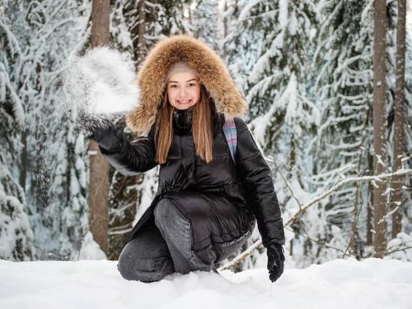 Uma mulher sorridente feliz em um capuz de pele em sua cabeça joga neve em você. — Fotografia de Stock