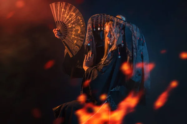 Un personaje de estilo asiático en un kimono y un sombrero de paja con cintas entre el fuego —  Fotos de Stock