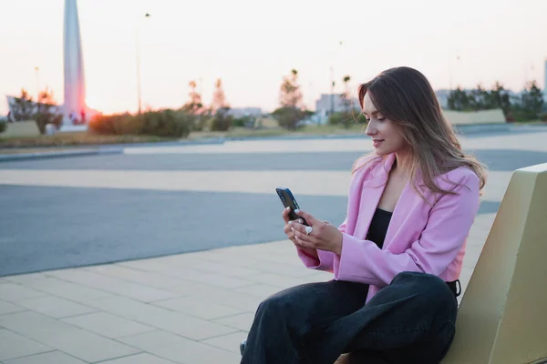 穿着粉色夹克的漂亮迷人的黑发女人用智能手机交流 — 图库照片