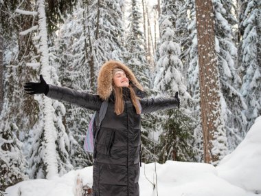 Başında bir kukuleta olan mutlu bir kadın doğayı kucaklıyor..