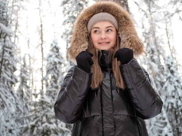Junge Frau in winterlicher Daunenjacke mit Fellkapuze spaziert im Winter im Wald — Stockfoto