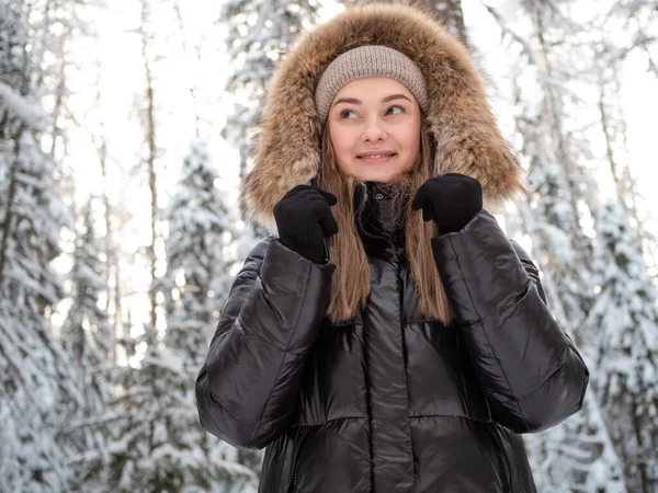 Giovane donna in un piumino invernale con cappuccio di pelliccia passeggiate nella foresta in inverno — Foto Stock