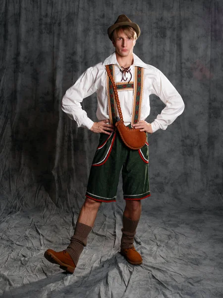 A young man in a national Bavarian suit with shorts on suspenders and a hat. — Stock Photo, Image