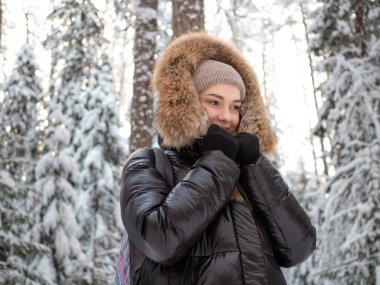 Kışın ceketli, kürklü genç bir kadın kışın ormanda yürüyor.