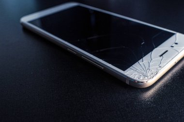 Kötü çatlamış ekranı olan ince beyaz bir akıllı telefon düşerken hasar görmüş..