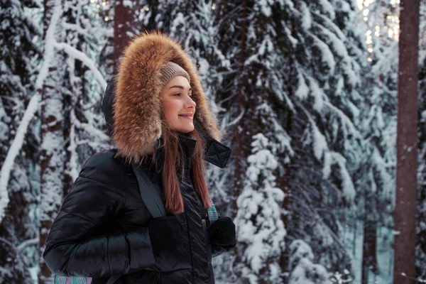 Wanita muda dalam jaket musim dingin dengan kerudung bulu berjalan di hutan di musim dingin — Stok Foto