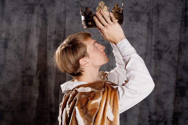 A young king in a fur robe crowns himself, a man holds a crown over his head.