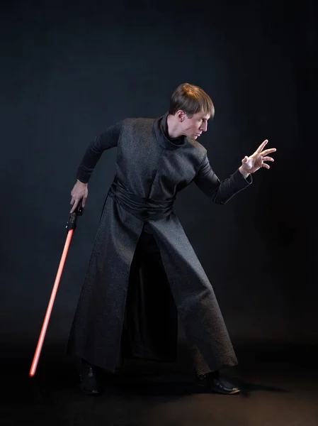 A villain with a red lightsaber, a young man in a long robe does fighting poses, — Stock Photo, Image