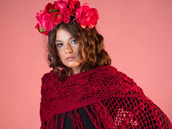 Eine helle und mutige junge Frau mit Rosen auf dem Kopf und einem roten Strickumhang. — Stockfoto